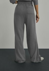 Grå brede sweatpants med elastisk talje, der har en baglomme og en blød tekstur, designet til komfort og afslappet brug.