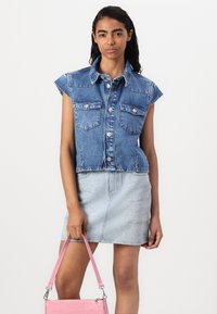 Denim mouwloos shirt met twee borstzakken, lichtblauwe minirok met kleine stippenpatronen, en een roze handtas met schouderband.