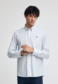 Knappad skjorta i ljusblå och vita ränder, i bomullsmaterial, långärmad med knäppning vid ärmsluten och en liten broderad logotyp på bröstet.