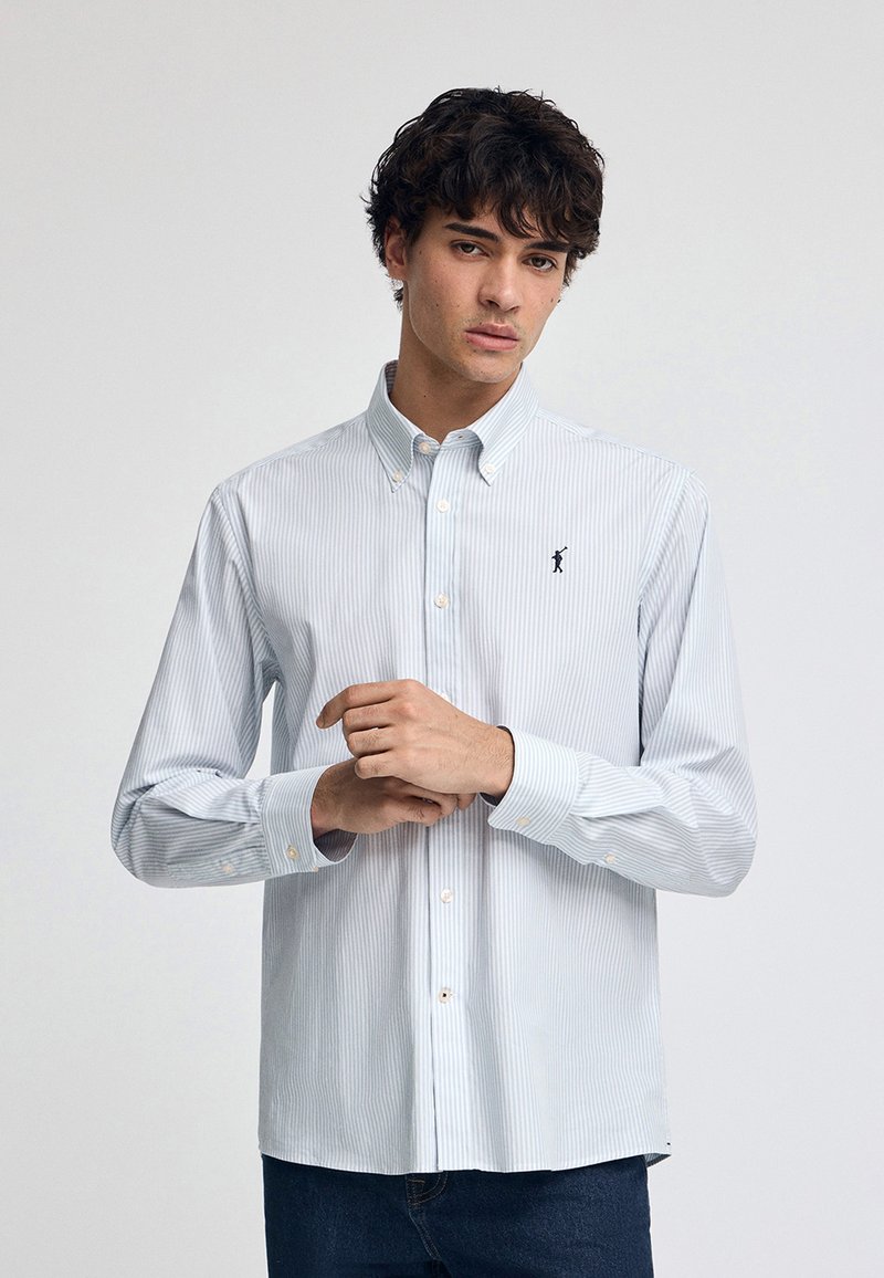 Knappad skjorta i ljusblå och vita ränder, i bomullsmaterial, långärmad med knäppning vid ärmsluten och en liten broderad logotyp på bröstet.