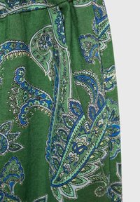 Tissu vert avec des motifs floraux cachemire détaillés en bleu, blanc et noir, montrant la texture et une couture froncée.