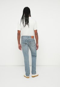 Svetlo modri denim kavbojke s ravnim krojem, z usnjeno oznako na pasu in diskretnimi šivi. Nosi se z belim T-shirtom.