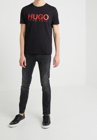 Svart bomullströja med röd text "HUGO HUGO BOSS". Kombinerad med mörka jeans och svarta sneakers. Enkla crew neck-design, slim fit.