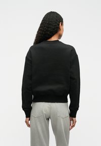 Černá mikina s kulatým výstřihem a ribovanými manžetami, s hladkým povrchem. Nosit s světle šedými džínami s vysokým pasem.