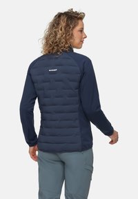 Mörkblå jacka med en puffig isolerad rygg i quilterat mönster, långa ärmar, figursydd passform och logotypdetalj på övre ryggen.