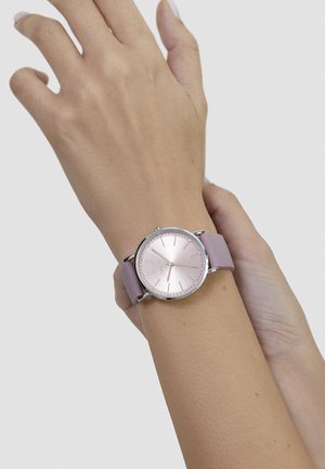 Runde Uhr mit einem rosafarbenen metallic Zifferblatt und silbernen Akzenten. Das Armband ist aus weichem, violettem Silikon. Verfügt über minimalistische Stundenmarkierungen und Zeiger.