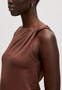 Bruin mouwloos topje met een draperende schouderontwerp, gemaakt van zachte, rekbare stof. Glad textuur met minimale naden.