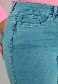 Niebieskie jeansy z denimu o gładkiej fakturze, z wysokim stanem i przednimi kieszeniami. Zawierają metalowe akcenty i detale z kontrastującym przeszyciem.