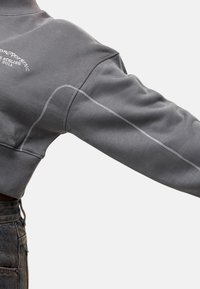 Felpa grigia a girocollo con collo alto e cuciture bianche a contrasto. Presenta una vestibilità rilassata e una consistenza morbida, ideale per un abbigliamento casual.