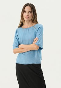 Lysblå chambray top med korte ærmer, rund halsudskæring og afslappet pasform. Bæres med en ensfarvet sort nederdel med glat tekstur.