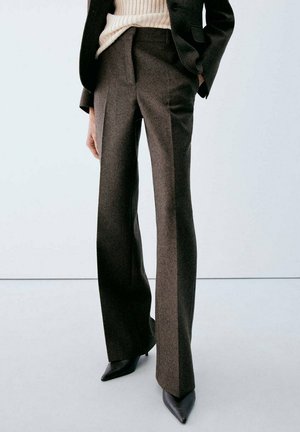 Personne portant un pantalon marron tailleur à jambes larges, des talons noirs à bout pointu, un blazer noir et un pull côtelé crème.