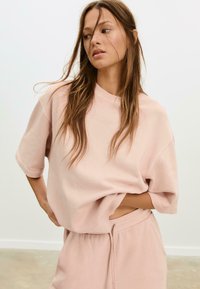 Helles rosa Oversize-Sweatshirt mit kurzen Ärmeln und Rundhalsausschnitt, kombiniert mit passenden Shorts mit Kordelzug aus weichem Stoff.