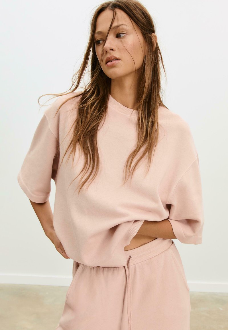 Helles rosa Oversize-Sweatshirt mit kurzen Ärmeln und Rundhalsausschnitt, kombiniert mit passenden Shorts mit Kordelzug aus weichem Stoff.