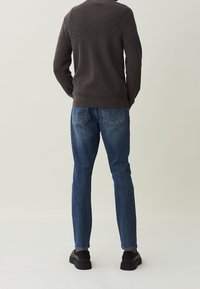 Tmavě šedý žebrovaný svetr spárovaný s modrými džínami. Černé boty doplňují celkový outfit. Pohled je zezadu, ukazuje zadní část oblečení.