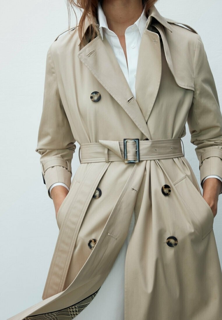 Trench coat beige con vita alta, grandi bottoni e tessuto leggermente texturizzato. Presenta un classico design doppiopetto e colletto a rever.