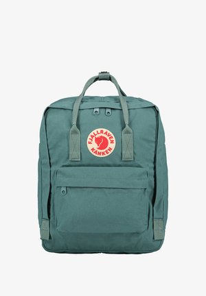 Sac à dos en tissu vert de forme rectangulaire, avec un écusson logo, une poignée supérieure et des bretelles ajustables. Il comprend une poche zippée à l'avant et un matériau texturé.