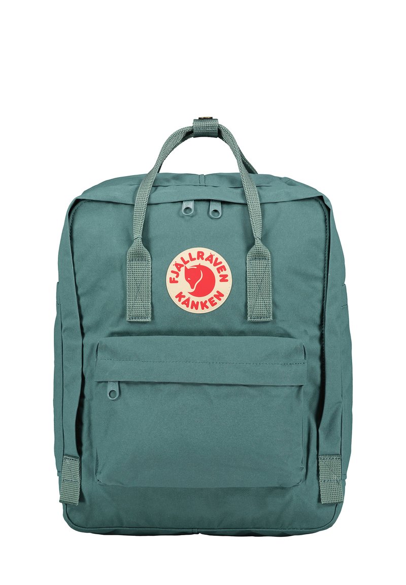 Sac à dos en tissu vert de forme rectangulaire, avec un écusson logo, une poignée supérieure et des bretelles ajustables. Il comprend une poche zippée à l'avant et un matériau texturé.