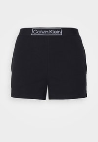 Fekete rövidnadrág puha textúrával és rugalmas derékpánttal, fehér "Calvin Klein" logóval. Egyenes vonalú, varrt szegéllyel.