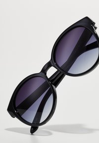 Ochelari de soare supradimensionați, de culoare neagră, cu lentile degradate care trec de la mov închis la deschis. Formă rotundă, cadru din plastic elegant și brațe drepte.
