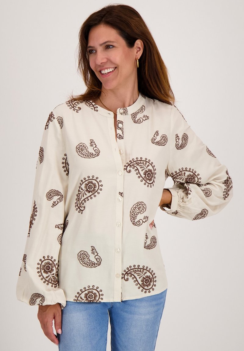 Langsleeve overhemd in crème met bruine paisley- en bloemenpatronen. Heeft een bandkraag enGathered mouwen voor een ontspannen pasvorm.