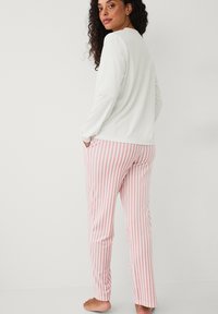 Witte lange mouwen top gecombineerd met roze en witte gestreepte broek. De broek heeft een losse pasvorm en zijzakken, afgewerkt met een rechte pijp.