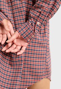 Chemise à carreaux rouge, bleu et beige en tissu au toucher doux, avec des boutons sur les manches et une coupe décontractée.