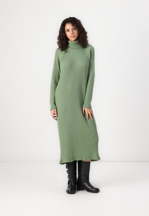 Robe tricotée vert à côtes avec un col roulé haut, des manches longues et une silhouette droite, assortie à des bottes noires à hauteur de genoux.