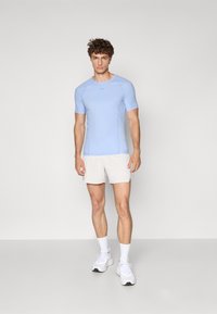 Lyseblå kortermet treningsskjorte med en tettsittende design, med mesh-sidelapper, kombinert med hvite shorts og hvite joggesko.