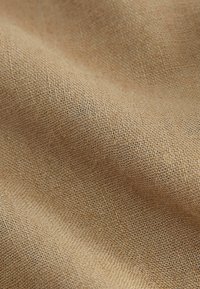 Tessuto beige con texture e motivo intrecciato, che mostra un aspetto morbido e naturale, adatto per applicazioni di tappezzeria o abbigliamento.