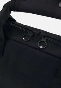 Gros plan sur un sac en tissu noir avec deux tirettes de fermeture éclair rondes et une poignée rembourrée enveloppée de matériau noir.