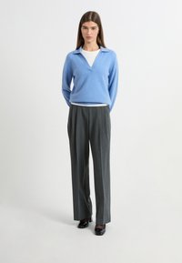 Jasnoniebieski sweter w serek wykonany z miękkiego materiału, nałożony na białą koszulę. Dobrany z taliowanymi szarymi spodniami i czarnymi szpilkami.