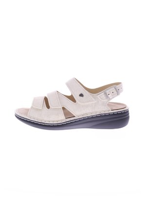 Light beige sandal featuring three Velcro straps, open toe design, cushioned footbed, and a curved black outsole. Accented with a small logo.