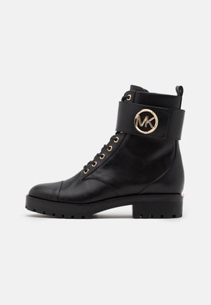 Bottines en cuir noir avec une semelle épaisse, des œillets dorés et une bride ornée d'un logo à la cheville. Texture lisse et bout rond.