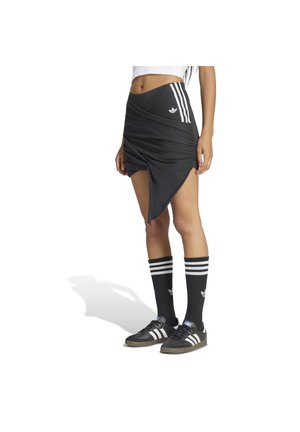 Mujer con una falda negra asimétrica con rayas blancas, calcetines negros Adidas y zapatillas negras Adidas con rayas blancas.