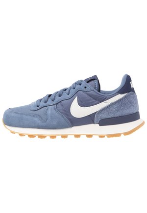 Baskets Nike bleues avec swoosh blanc, dessus en suède et tissu, design à lacets, col rembourré et semelle en caoutchouc naturel.