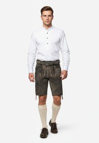 Läderhosen i mörkgrått med ljusa sömmar, i kombination med en vit långärmad skjorta och krämfärgade knälånga strumpor. Bruna skor avslutar looken.
