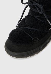 Gros plan sur une botte noire texturée avec des lacets et des œillets en métal, dotée d'une semelle épaisse en caoutchouc, sur fond blanc uni.