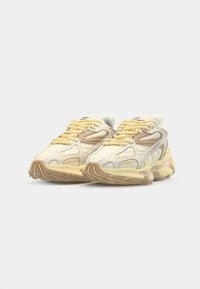 Baskets Lacoste présentant un schéma de couleurs crème et jaune, des matériaux en mesh et cuir, une semelle rembourrée et des accents latéraux distinctifs.