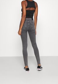 Höga, figurnära grå skinny jeans med två bakfickor. Bärs tillsammans med en svart ärmlös topp och svarta kanvas sneakers.