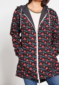 Czarna kurtka przeciwdeszczowa z fantazyjnym wzorem w czerwono-niebieskie łodzie i fale, z kapturem, białym zamkiem błyskawicznym i elastycznymi mankietami. Lekka tkanina.