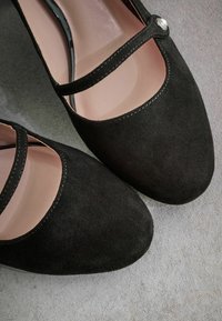 Pantofi Mary Jane din suede negru, cu vârf rotund, două curele subțiri și un accent decorativ asemănător unei perle lângă cataramă. Două linii interioare netede.