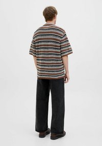 Chemise à manches courtes rayée en fil marron, noir et blanc, avec une coupe décontractée et un design en tricot texturé. Portée avec un pantalon large noir.