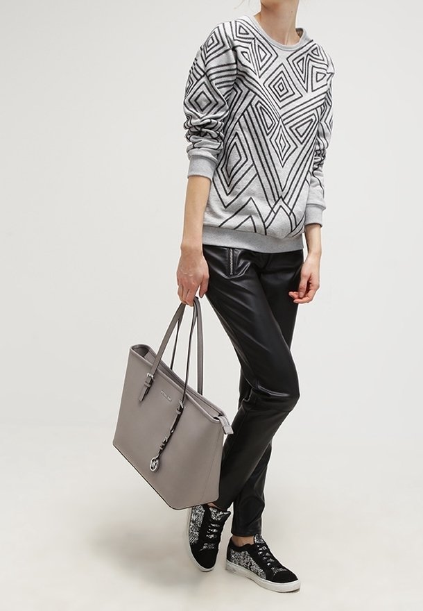 Sweatshirt gris avec un motif géométrique noir, pantalon en cuir synthétique noir, sac en toile gris et baskets noires à motif.