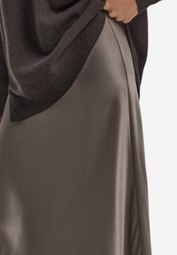 Ciemnoszary dzianinowy sweter o szerokim dekolcie w połączeniu z gładką, satynopodobną oliwkowozieloną spódnicą z bocznym rozcięciem.