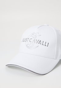 Cappellino da baseball bianco con ricamo grigio che presenta il logo "JUST CAVALLI", design strutturato e una superficie lucida e liscia sul fronte.
