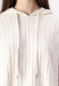 Helle beige Kapuzenpullover mit senkrechter Rippstruktur. Verfügt über Kordeln mit metallischen Spitzen und einen lässigen Schnitt.