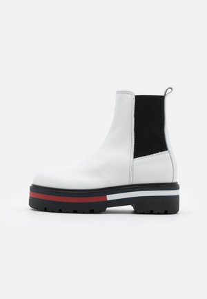 Białe skórzane botki za kostkę z czarnymi elastycznymi panelami bocznymi, teksturowanym wierzchem, pętlą do zakładania oraz kontrastującą podeszwą z platformą z czerwonymi i niebieskimi paskami.