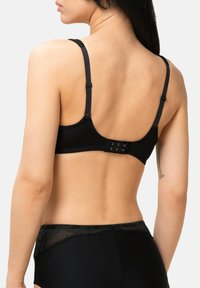 Černá podprsenka s nastavitelnými ramínky, hladkým materiálem a zapínáním na háček a oko. Obsahuje krajkové detaily podél obvodu. Zadní pohled ukazuje střih a design.