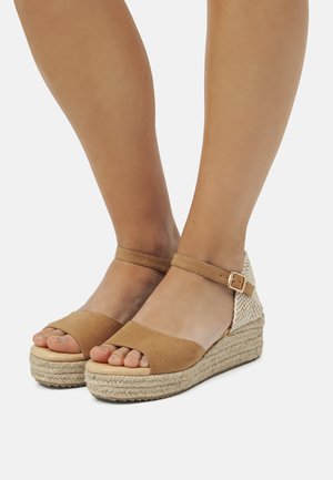 Tan-Wedgesandalen mit einem weichen Wildlederfinish, offener Zehenpartie und einem gewobenen Textilabsatz. Schnallenriemen für einen sicheren Halt. Jute-Seil-Details an der Sohle.