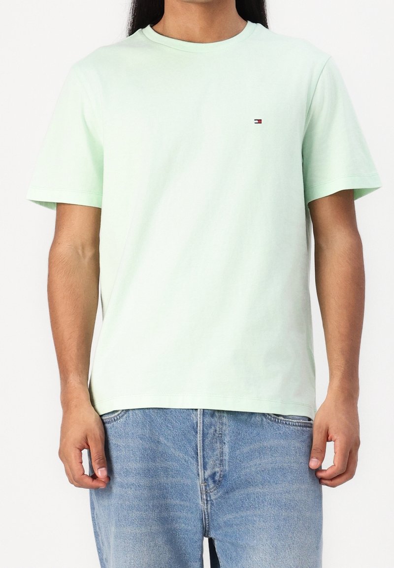 T-shirt en coton vert clair à manches courtes, col rond, avec un petit logo sur la poitrine. Associé à un jean en denim bleu clair.